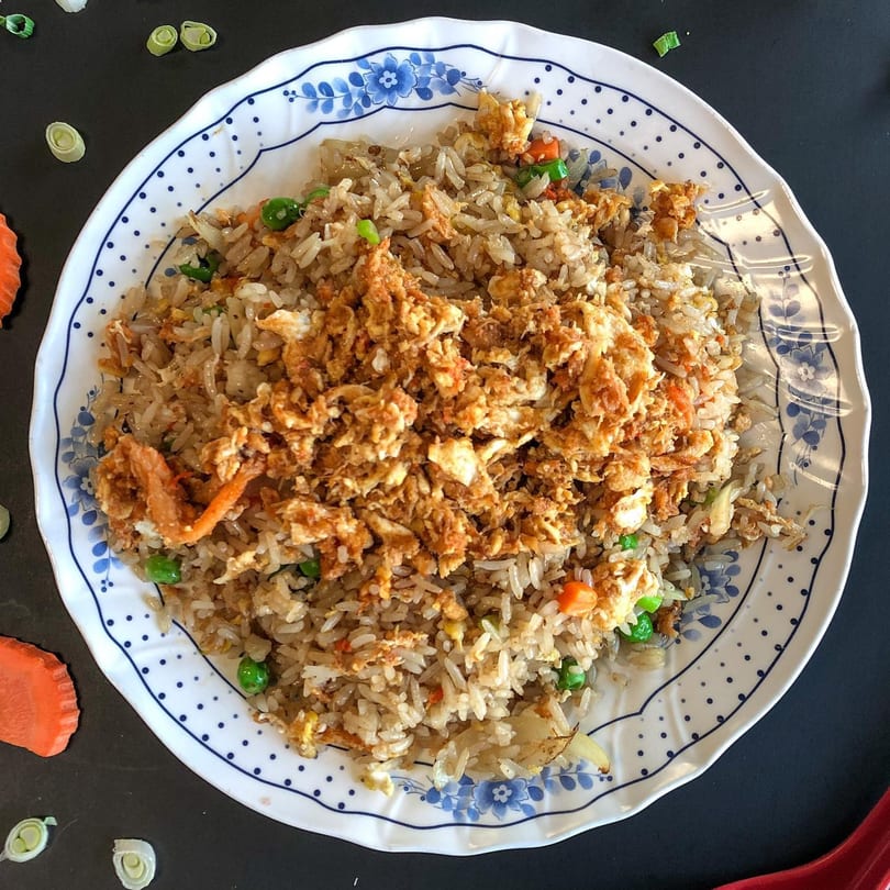 Thai Nary BBQ's fried rice with scrambled egg, peas, and carrots on a blue and white plate.