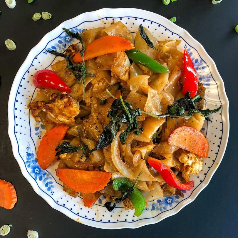 Close-up of Thai Nary BBQ's Pad See Ew with wide noodles, carrots, peppers, and basil.