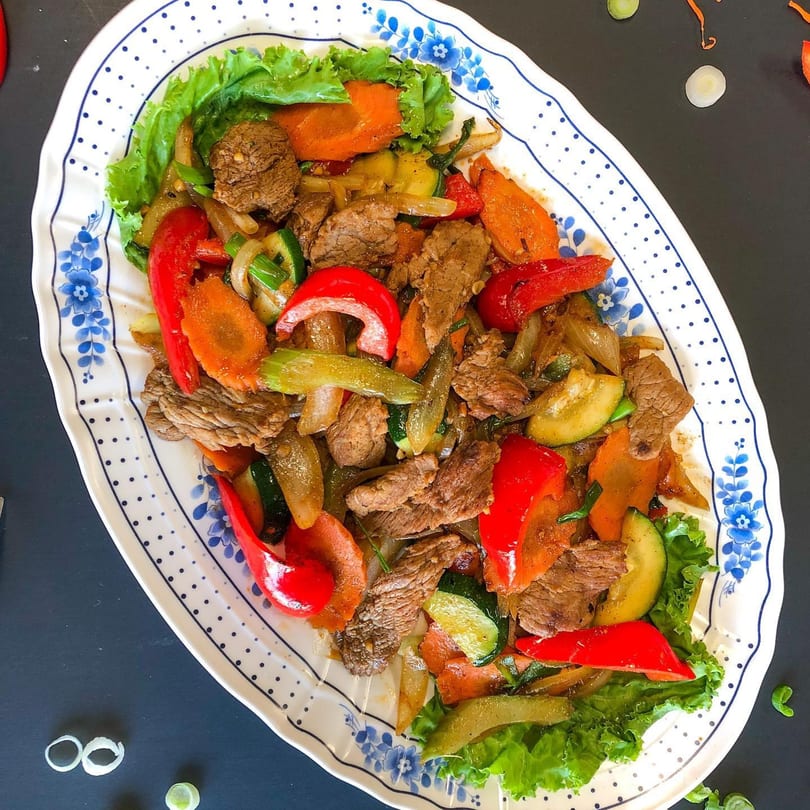 Thai Nary BBQ's stir-fried beef with colorful bell peppers, carrots, zucchini, and onions on a decorative platter.